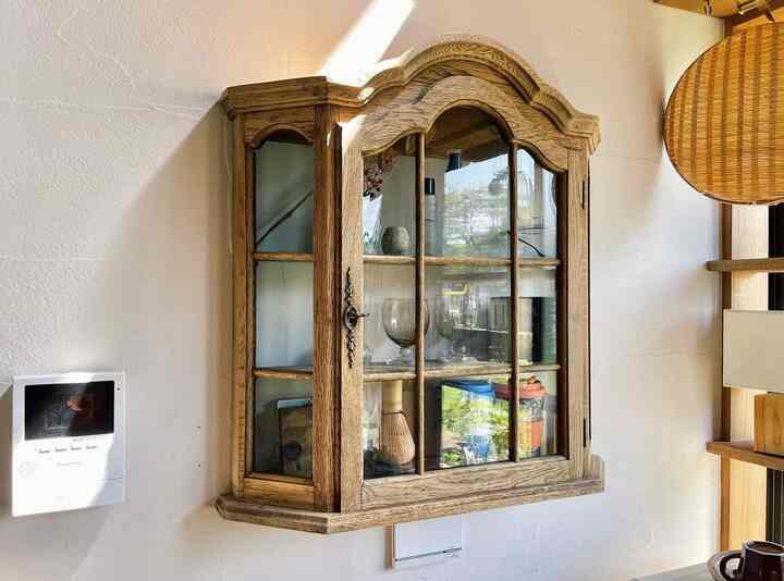 ナチュラルな色調のキッチンの壁に、フレンチアンティークスタイルの木製とガラスのキャビネットが配置された雰囲気のあるインテリア