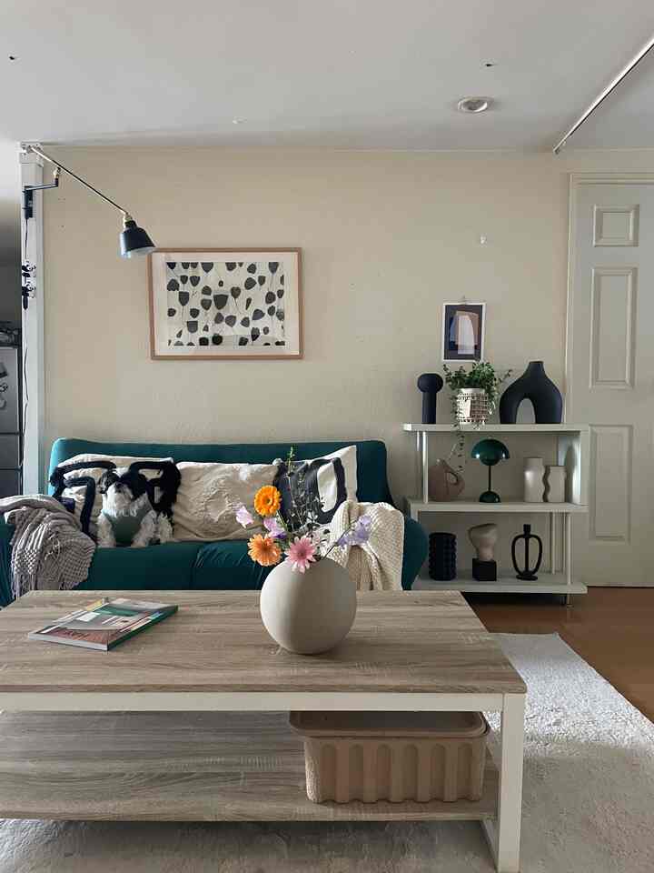 グリーンのソファとウッドトーンのテーブルが配置されたモノトーンのリビング、ソファに座る犬がいる落ち着いた空間