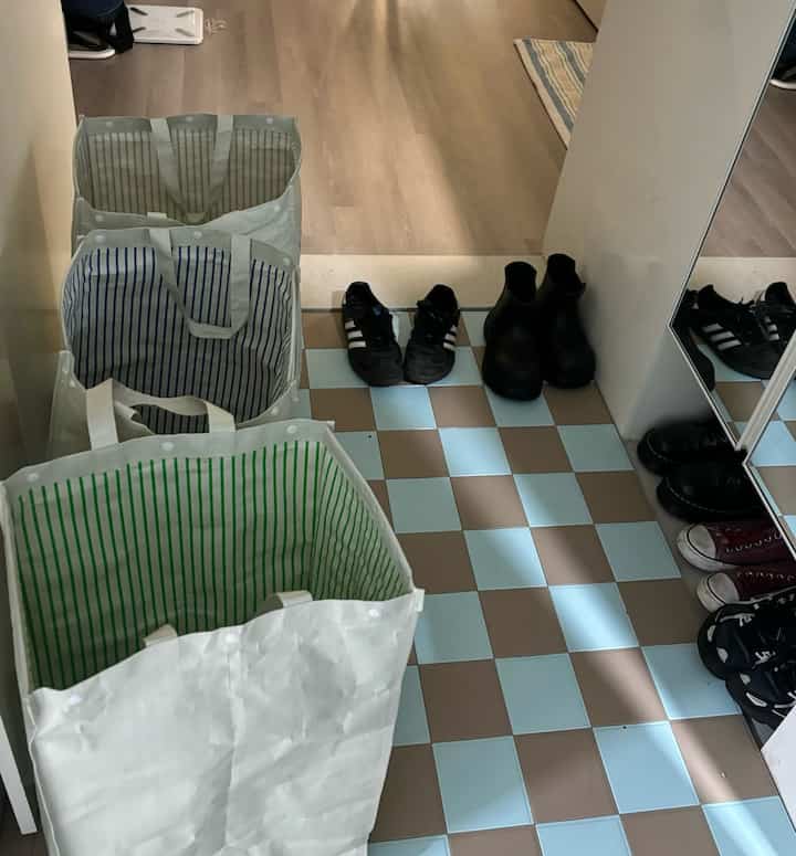 ミントとブラウンの市松模様タイルの玄関に、三つの縞模様の分別ゴミ箱と整頓された靴が配置された印象的な空間