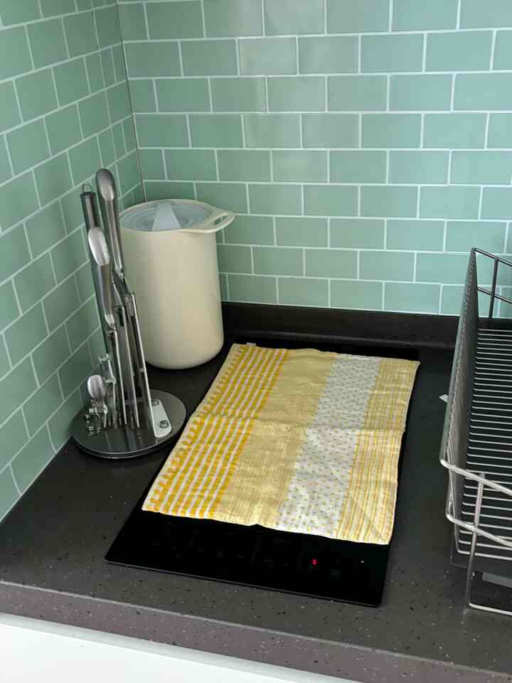 淡い緑色のタイルと黄色いタオルが配置された清潔感のあるキッチンのインテリア。