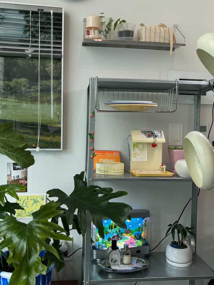 ホワイトとグレーのトーンのベランダ空間、金属製の棚と多様な植物やインテリア小物が配されたコンパクトでモダンな雰囲気のあるインテリア