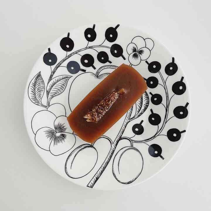 白地に黒の花柄の皿の上に茶色のゼリーが載ったアラビアの皿、白い面に配置された