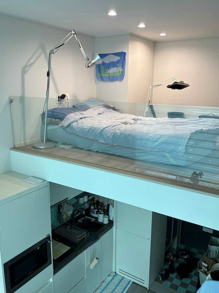 ホワイトとブルーのトーンが特徴のワンルームロフト、寝室とキッチンが調和した洗練された空間