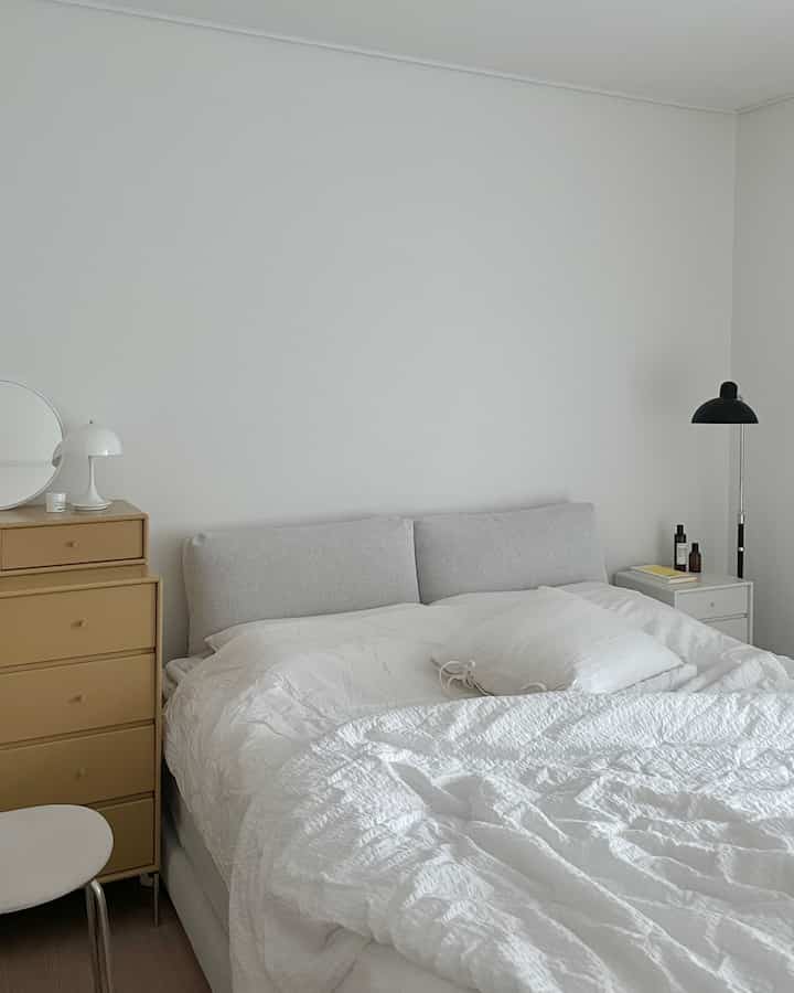 白とベージュの色調の寝室、中央に大きなベッドと左側にベージュのチェストが配置されたモダンな空間