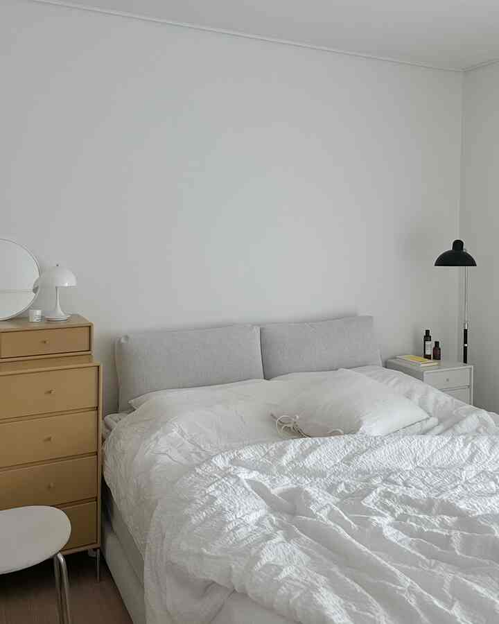 白と茶色のトーンの寝室、大きなベッドとナイトテーブル、ドレッサー、フロアランプが配置されたシンプルな雰囲気のインテリア