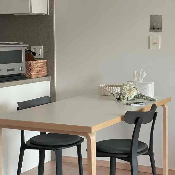 ホワイトとブラウンのナチュラルトーンのダイニング、ダイニングテーブルと2つの黒い椅子が配置されたミニマルな空間