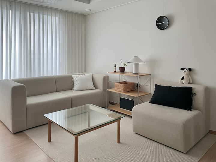 白とナチュラルの色調のリビング、シンプルでモダンなソファとユニット棚、ガラスのコーヒーテーブルが配置された清潔感のあるインテリア