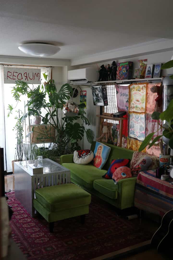 緑のソファと大きな植物が配置された赤いラグのある自然なリビング空間