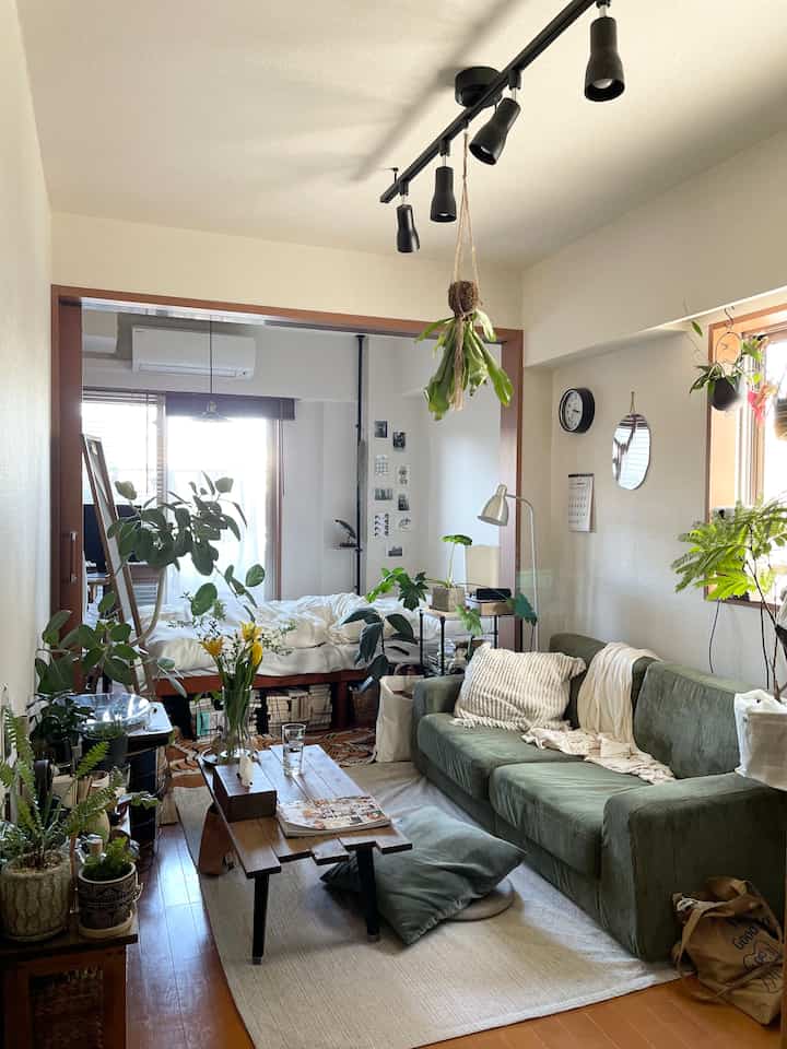 ナチュラルなトーンのワンルームのリビングルーム、緑のソファと多彩な植物が配置された雰囲気ある空間