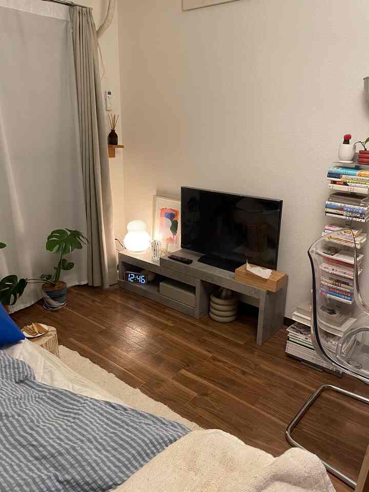 ナチュラルな木目調の床とテレビ台があるリビング、透明な椅子と植物が配置されたシンプルでモダンな雰囲気の空間