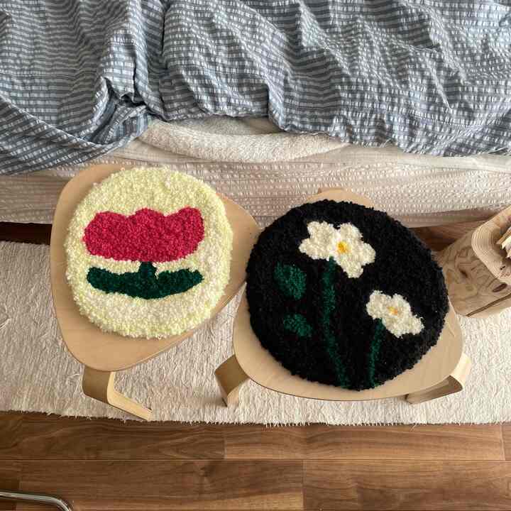 木目調のスツールの上に花柄のパンチニードルクッションが置かれた、ベッド横のナチュラルスタイルの寝室空間