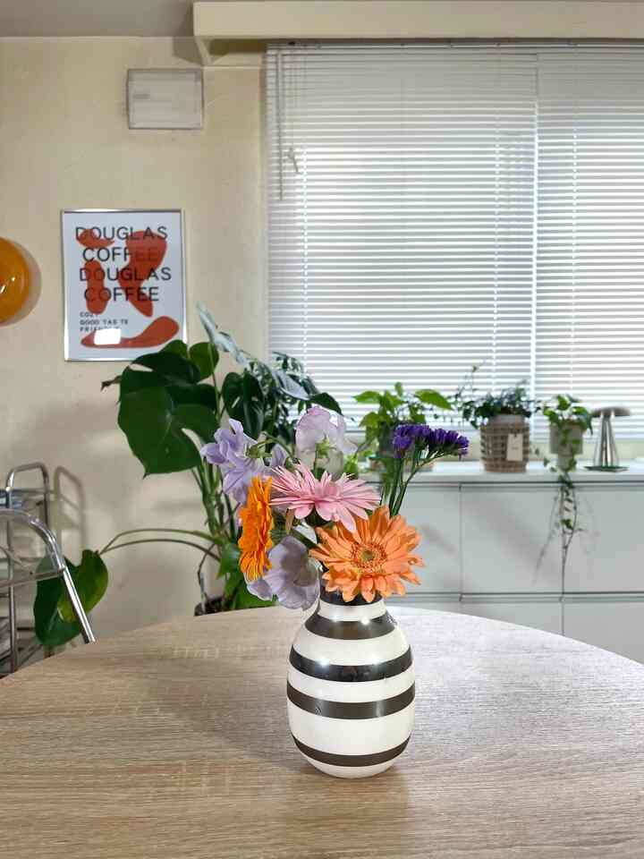 ナチュラルカラーと白を基調としたキッチン空間、中央のテーブルにストライプの花瓶と花が置かれた雰囲気のあるインテリア