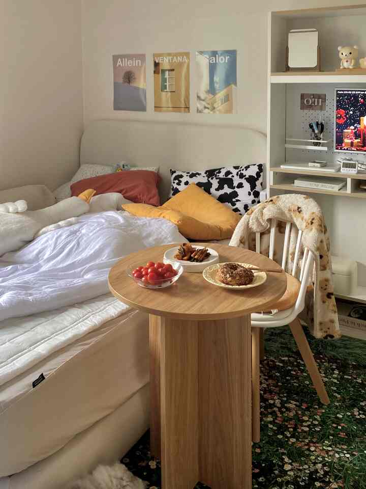 ホワイトとウッドトーンの調和した寝室、丸い木製テーブルと花柄ラグがポイントの暖かみのあるインテリア