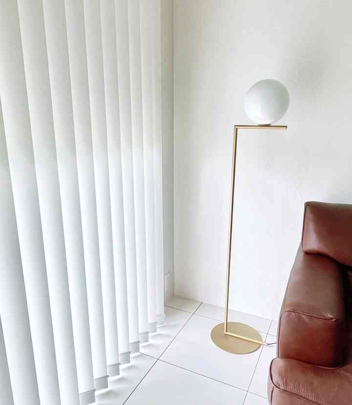 白とゴールドの配色が印象的なリビング、ブラウンのソファとフロアランプが配置されたモダンで清潔感のある空間