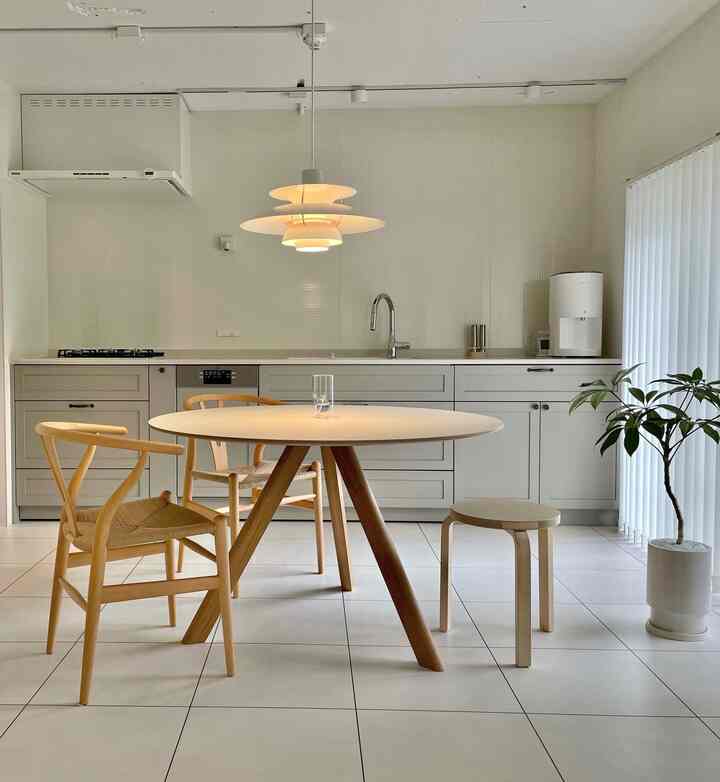 白と木目調のキッチン、シンプルで北欧風の丸いダイニングテーブルと椅子が配置された温かみのある雰囲気のインテリア