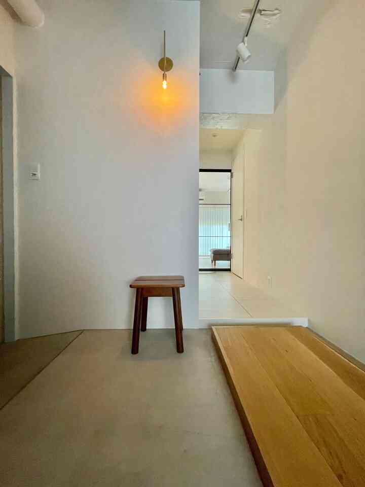 ナチュラルカラーの玄関スペース、木製スツールと黄色のブラケットライトが調和した清潔感のあるモダンなインテリア