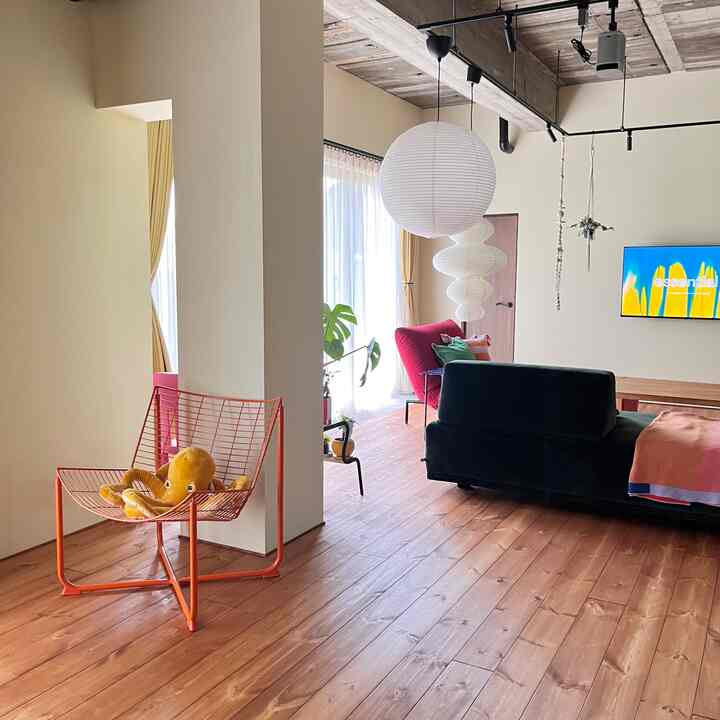 ナチュラルな木床とベージュの壁が調和したリビング、黒いソファとオレンジのアームチェアがアクセントの温かみのある空間
