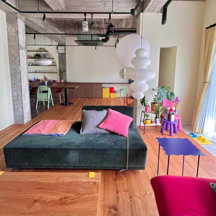 木目調の床とナチュラルトーンの壁のリビング、カラフルな子供用家具と大きなグリーンのソファが配置された雰囲気のある空間