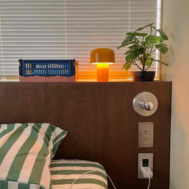 木目調の寝室、ストライプの寝具と黄色いランプ、緑の植物が配置された雰囲気のあるインテリア