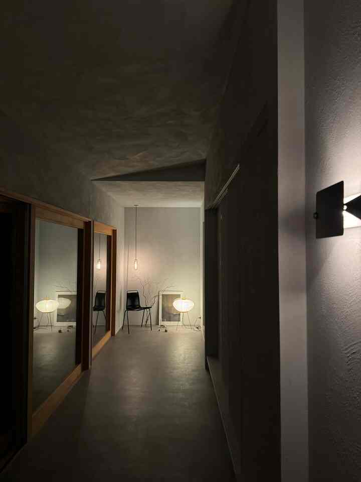 ライトグレーのモダンな玄関、壁の照明とテーブルランプが雰囲気を醸し出すシンプルな空間