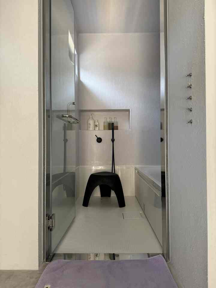 白を基調としたバスルーム、中央に黒いスツールと整然と並べられたバス用品が配置されたモダンな空間