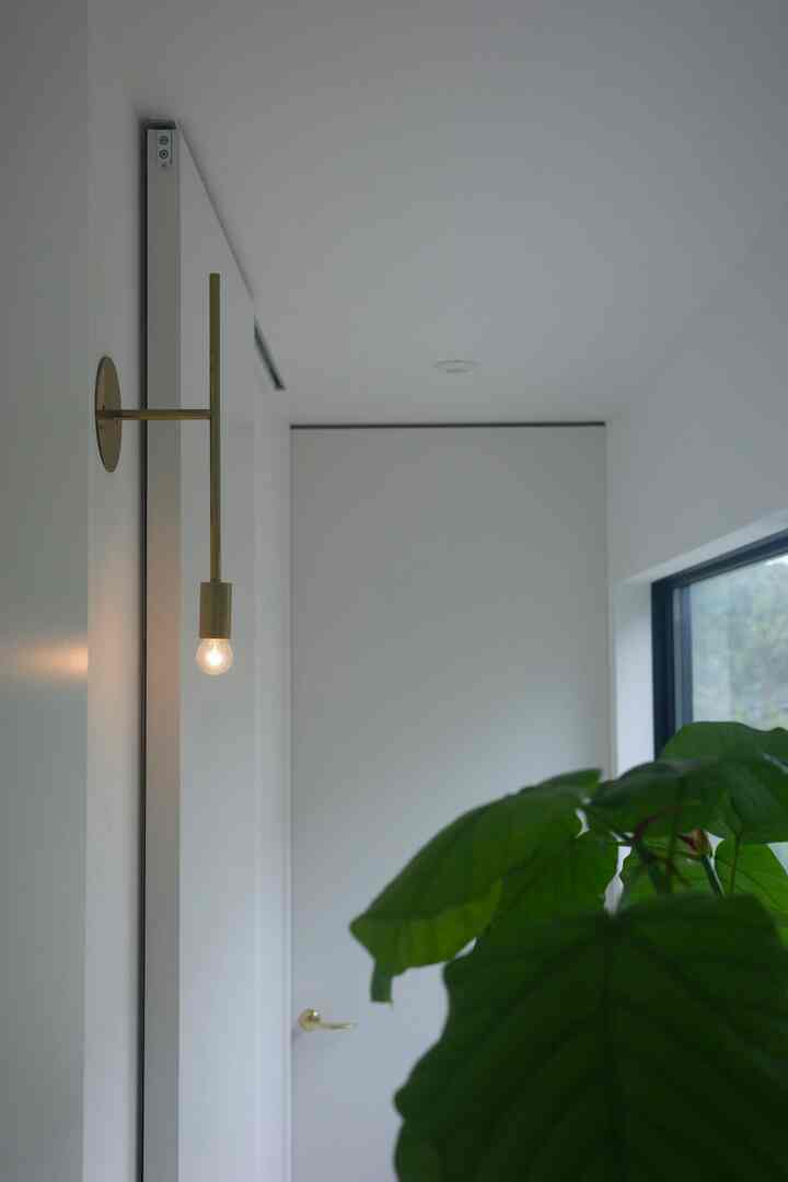 白い壁とゴールドのブラケットライトが配置された清潔感のある玄関、自然なグリーンの植物を配した印象的な空間