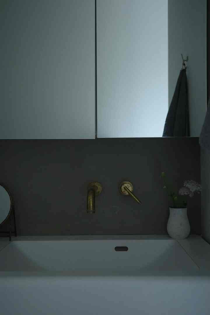 ホワイトとブロンズの調和が美しいミニマルなバスルーム洗面台、壁付け水栓が配置された清潔感のある空間