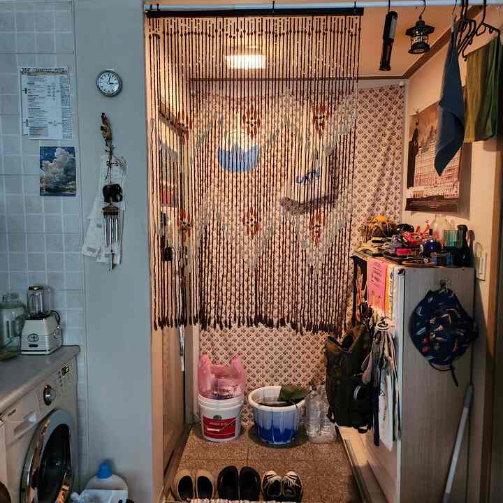 ブラウン調の玄関、木製ビーズのカーテンとペンキ缶のゴミ箱、プラントスタンドが配置された雰囲気のあるインテリア