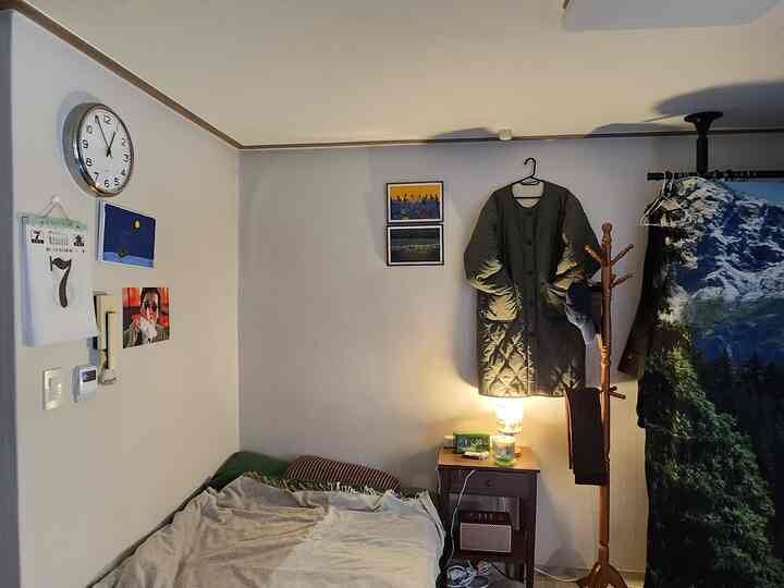 白い壁と茶色の木製家具が配置された寝室、ナイトテーブル上の照明とコートラックが印象的な空間