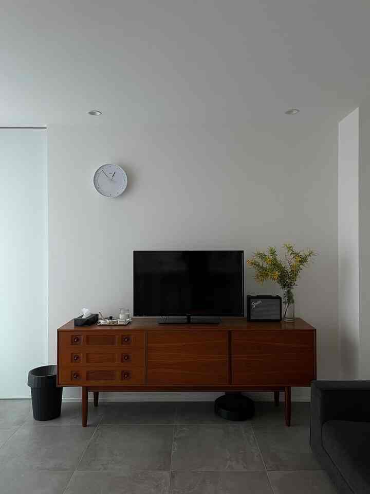 白い壁と中間色の茶色い木製サイドボードが配置されたシンプルでモダンなリビングスペース