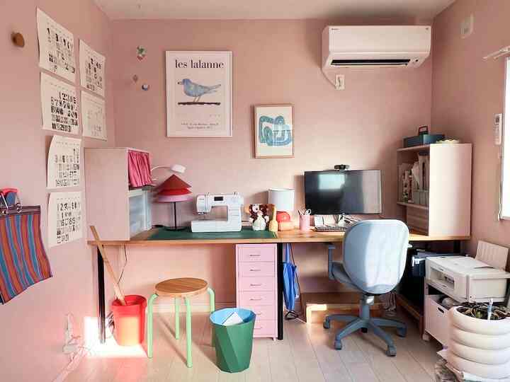 ピンク色の壁と清潔感のあるデスクが配置されたコンパクトなホームオフィス、オフィスチェアとコンピューターを備えたインテリア