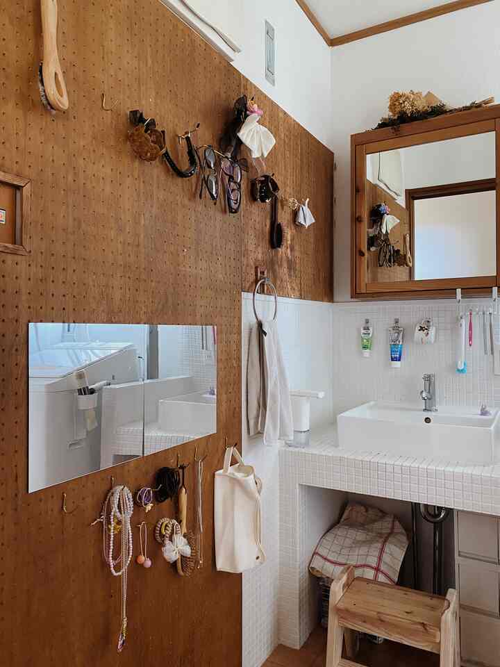 ナチュラルな木目調と白いタイルのコンパクトなお手洗い、壁に収納用の有孔ボードと鏡が配置された実用的なインテリア