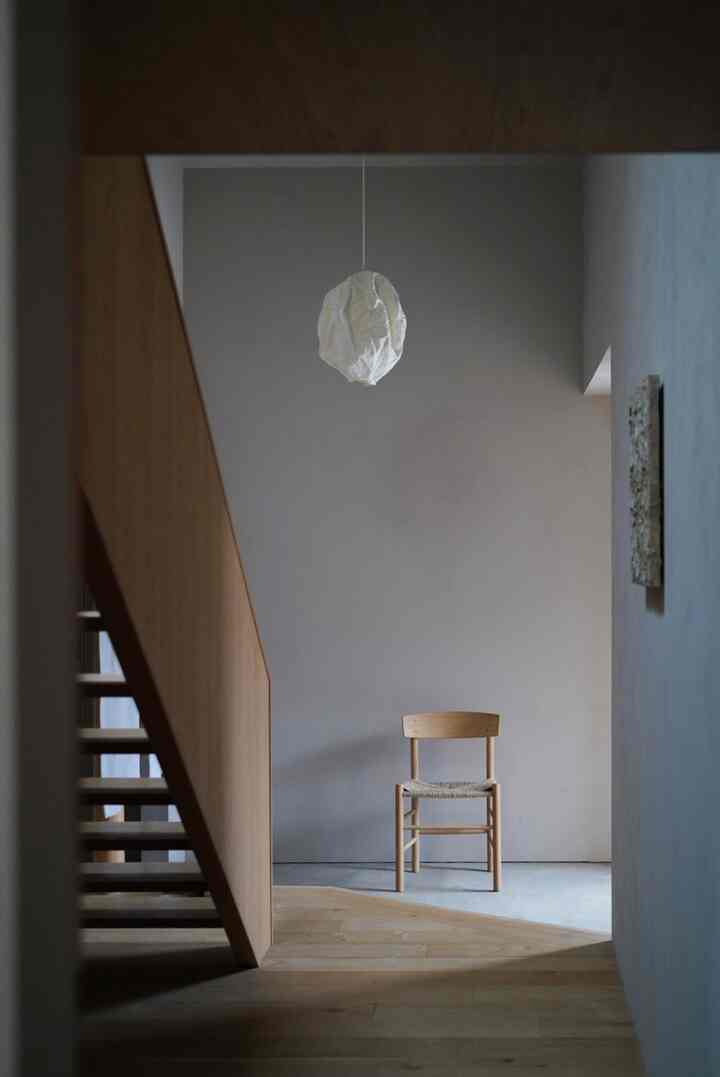 ナチュラルカラーの落ち着いた玄関空間、シンプルな木製椅子と穏やかなグレーの壁が配置されたミニマルなインテリア