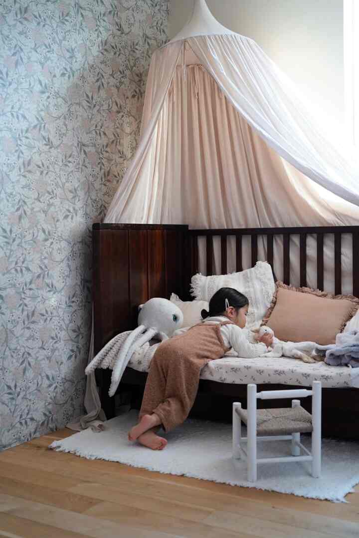ナチュラルなベージュ色調の子供部屋、改造されたベビーベッドのソファとキャノピーテントが居心地の良い雰囲気を演出するインテリア