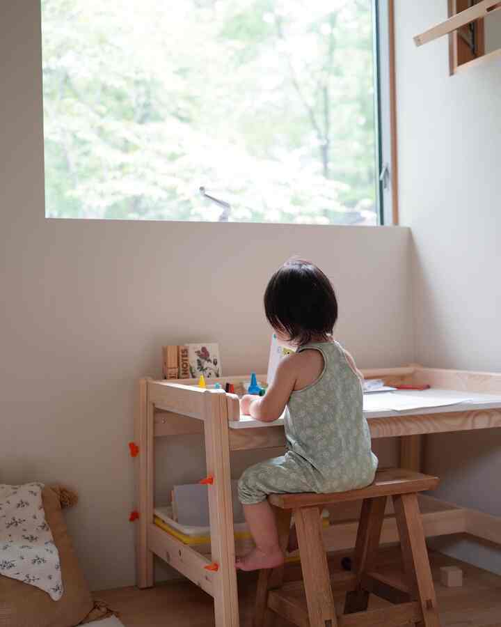 ナチュラルな木目調の子供部屋、窓辺に置かれたIKEAの子供用机とアンティークの木製スツールが配置されたシンプルな空間