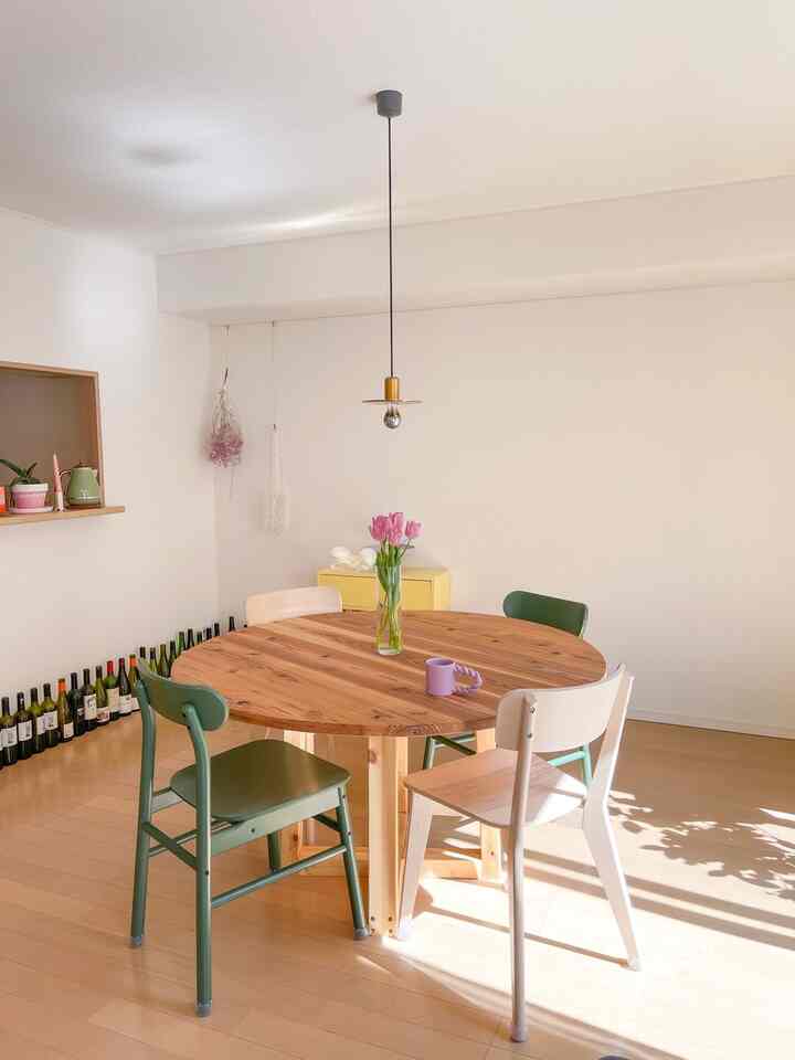 ナチュラルカラーとホワイトのダイニング、丸い木製テーブルと異なる色の椅子が配された雰囲気のあるインテリア