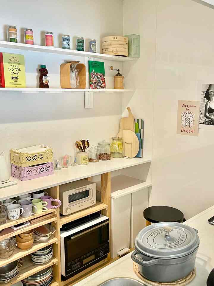 白い壁とナチュラルな木目調の棚がある小さなキッチン、整頓された収納アイデアとキッチン用品が配置された落ち着いた空間