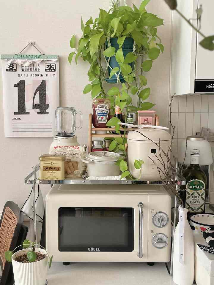 アイボリー色調のキッチンスペース、ミニ炊飯器とレトロ電子レンジ、植物が配置された雰囲気のあるおうちカフェ