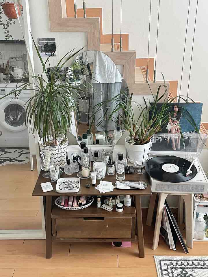 温かみのある木目調のリビング、大型不定形ミラーと植物、ミニキャンドルやターンテーブルが配置された雰囲気のある空間