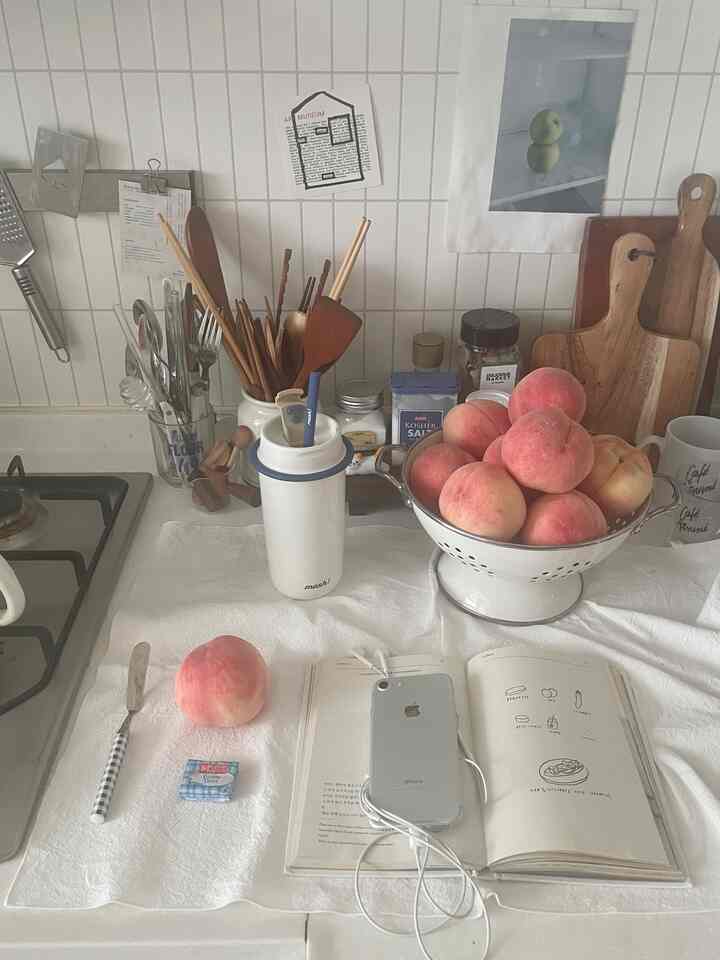 白いタイル壁とナチュラルな木製まな板が配置されたキッチンカウンター、桃と調理器具がある雰囲気のある空間