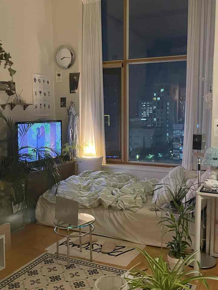 白と木目調が調和したコンパクトなリビング、中央にベッドとテレビ台が配置された雰囲気のある空間