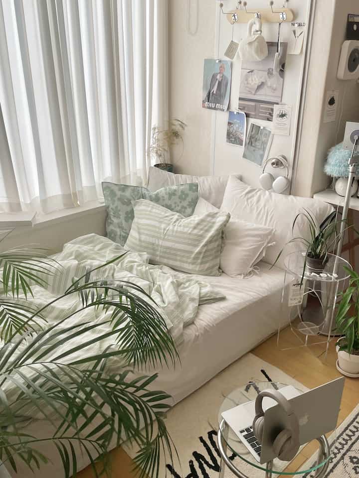 白と緑の色調の寝室、低いベッドとカーテン、植物が配置された自然で落ち着いた雰囲気のインテリア