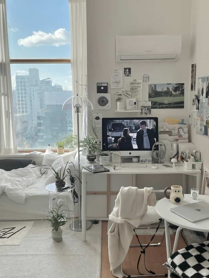 白を基調としたナチュラルモダンな小さな寝室。窓際にカーテンと植物が配置されたホームオフィスのある落ち着いたインテリア