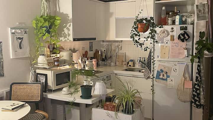 ナチュラルな色調と白いキッチン、小さな多目的ダイニングテーブルと多くの植物が配置された雰囲気のある空間