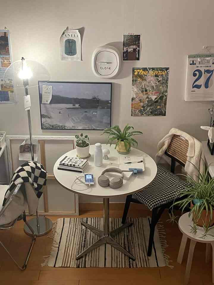 白を基調とした小さなダイニングルーム、丸テーブルとチェック柄の椅子、照明、植物、ポスターが配置されたモダンで温かみのあるおうちカフェ空間