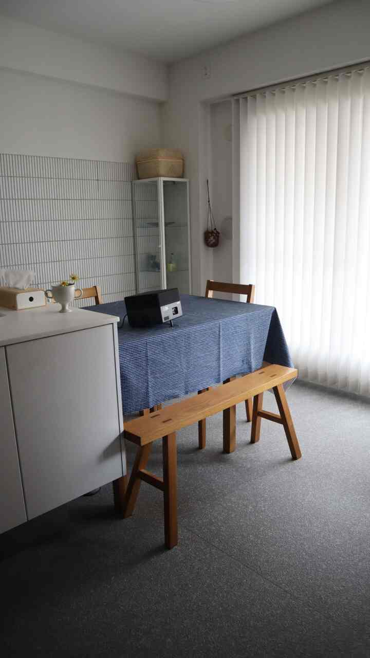 白とグレーのトーンのダイニングルーム、木製の食卓と椅子、テーブル上のプロジェクターが配置されたシンプルで抜け感のある空間