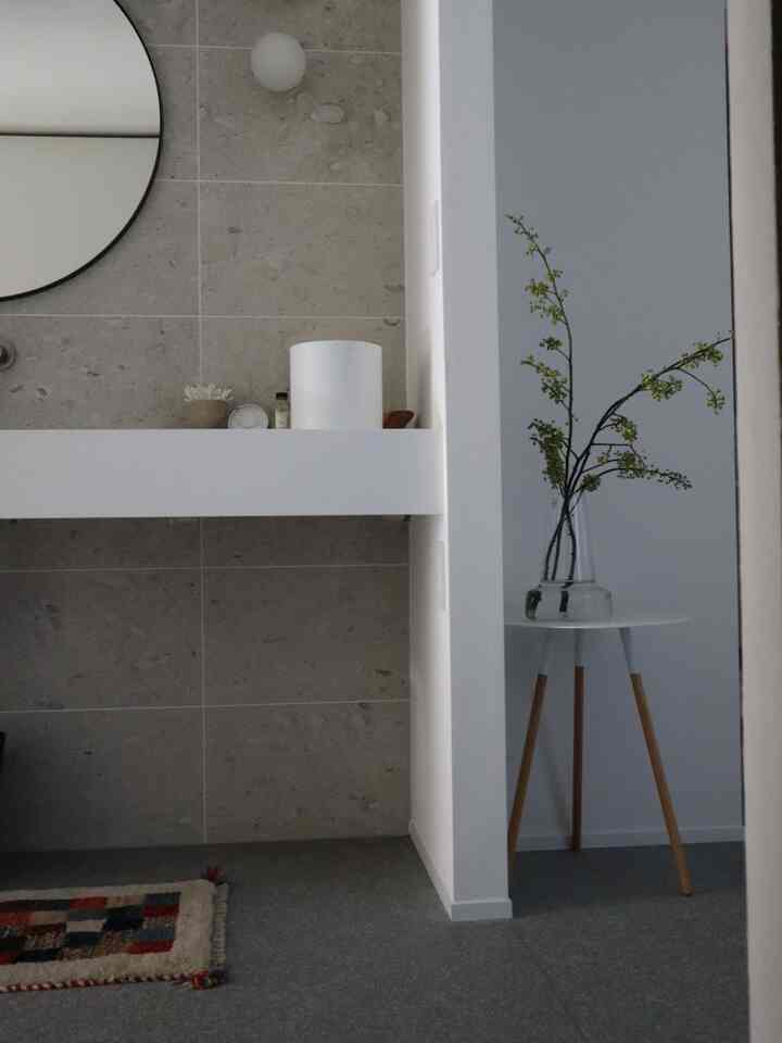 ナチュラルな色調のバスルーム、白い洗面台とL字型の棚の隣に花瓶が置かれたシンプルなインテリア