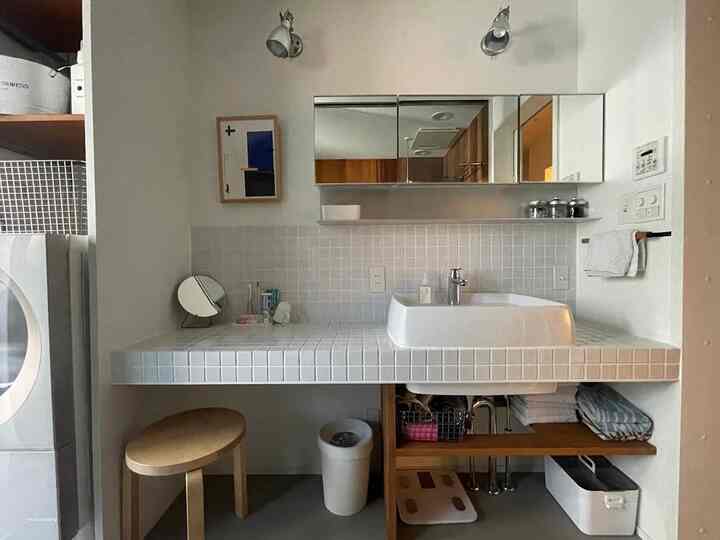 ホワイトとブラウンのナチュラルカラーのランドリールーム、ナチュラルモダンなスツールと鏡、収納が配された清潔感のあるインテリア