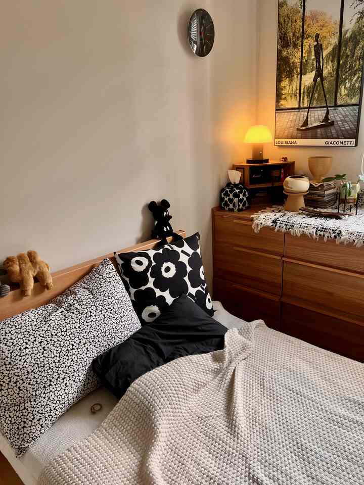 ホワイトとブラウンの色調の寝室、木製ベッドと寝具、ナイトテーブルの上にテーブルランプとインテリア小物が配置されたシンプルな空間