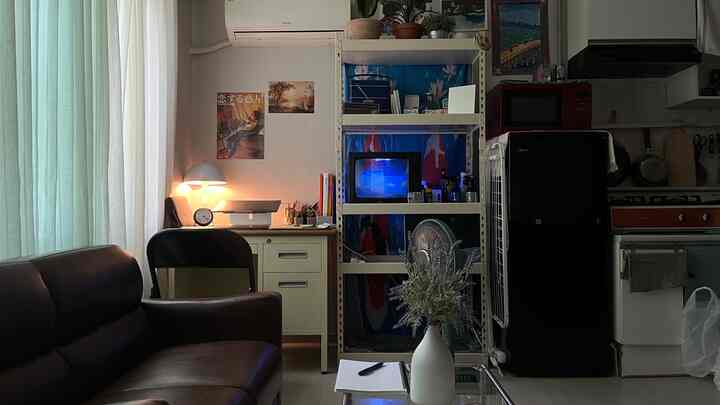 暗いブラウンのレザーソファがあるコンパクトなリビングルーム、白いデスクと棚が配置され、モダンな雰囲気のレトロなキッチンと調和した空間